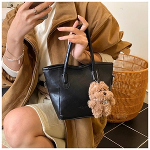 Detalle del bolso cubo de cuero negro con un colgante de perro de peluche marrón