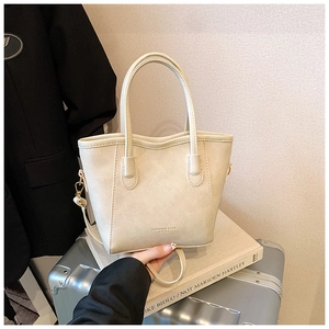 Detalle del bolso tipo cubo en cuero crema con asas dobles y estampado de moda