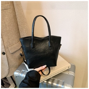Detalle de bolso tipo cubo de cuero PU negro con herrajes dorados sobre maleta