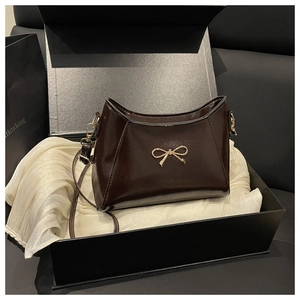 Dettaglio borsa in pelle verniciata marrone cioccolato con fiocco dorato in una confezione