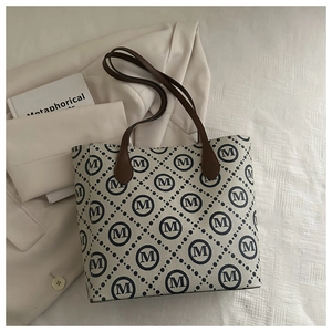 Vue à plat d'un sac cabas crème avec motif monogramme bleu et anses en cuir