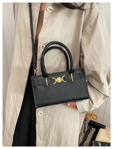Detail of elegant black leather handbag with a gold heart clasp shown on a model