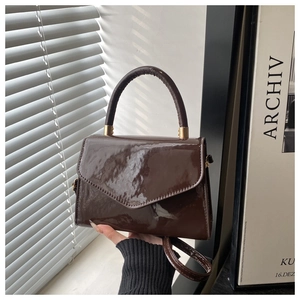 Close-up of glossy patent leather handbag in coffee brown with polished metal hardware