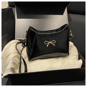 Dettaglio borsa a tracolla in pelle verniciata nera con fiocco dorato in confezione regalo