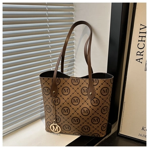 Gros plan du sac fourre-tout marron avec motif M et pendentif doré sur un rebord