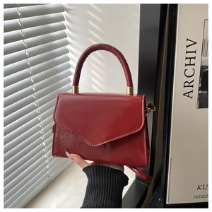 Detail of dark red glossy patent leather handbag with elegant handle and trapezoid flap