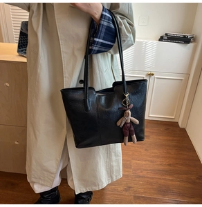 Detail of a large black faux leather tote bag with a cute rabbit doll charm attachment