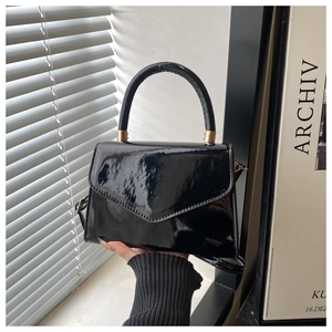 Detail of glossy black patent leather handbag with gold hardware and trapezoid design