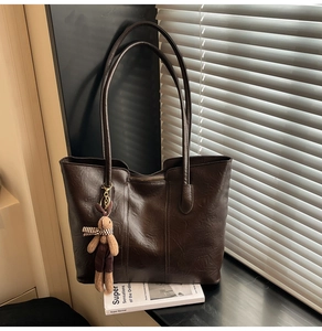 Detail of dark brown tote bag with leather texture, zipper, and cute rabbit pendant