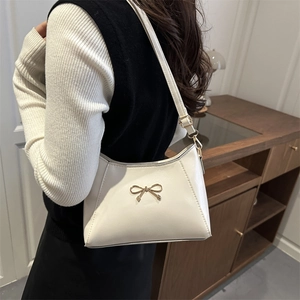 Borsa a spalla color crema con fiocco dorato indossata da una modella in un interno