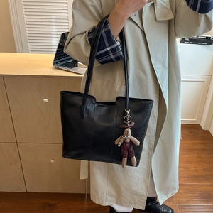 Large black leather tote bag with a cute rabbit charm shown in a cozy indoor setting