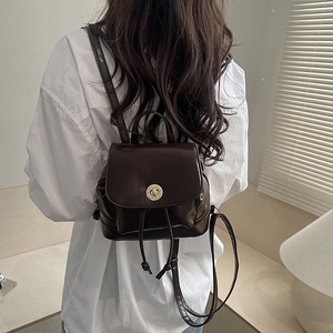 Deep brown faux leather mini backpack with gold twist lock shown on model wearing white shirt
