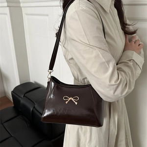 Borsa sottobraccio in pelle lucida caffè scuro con fiocco dorato, vista laterale su modella