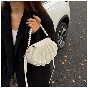 Detail of white quilted shell-shaped bag with pearl handle and golden hardware accent