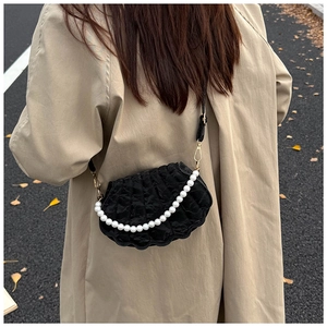 Detail of black pleated shell bag with white pearl chain on a beige coat background