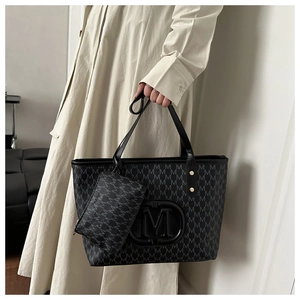 Detail of black tote bag featuring M-pattern print and matching small zip pouch accessory
