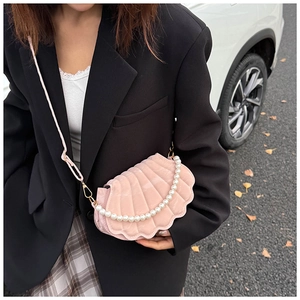 Outdoor shot of pink velvet shell bag with pearl handle and long crossbody strap on model