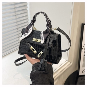 Macro shot of black crocodile embossed handbag with metallic turn-lock and silk scarf handle