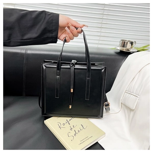 Détail d'un sac à main carré en cuir noir mat avec un long pompon décoratif sur sofa