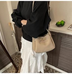 Detail view of beige pebble leather bucket bag with golden twist lock on a model