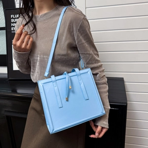 Sac à bandoulière carré bleu ciel aspect brillant avec pendentif doré sur modèle