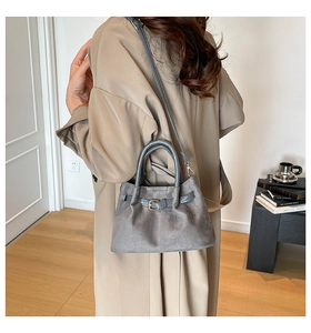 Model showing a gray suede bucket bag with metal buckle in a cozy indoor home setting