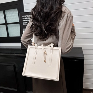 Sac à bandoulière carré en cuir crème minimaliste porté par un mannequin en scène
