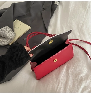 Detail of red rectangle crossbody bag with golden magnetic clasp on white fabric background
