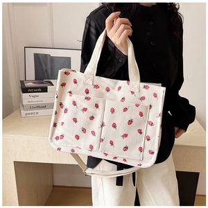 Detail of cream corduroy tote bag with strawberry print and dual front storage pockets