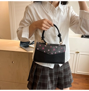 Detail of black PU crossbody bag featuring pink floral print and golden metal rings