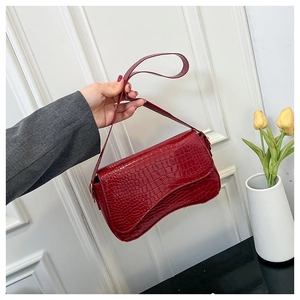 Close-up of deep red crocodile embossed leather shoulder bag held by a person