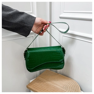 Green crocodile pattern baguette bag with unique curved flap detail held by a model