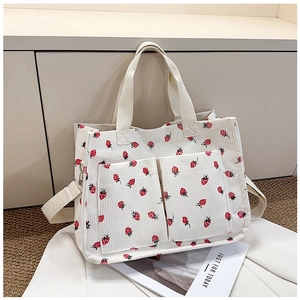 Detail of cream corduroy tote bag featuring red strawberry prints and front dual pockets