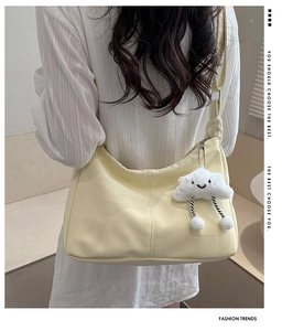 Detail of light yellow hobo bag with cloud plush charm worn by a model in a minimal setting