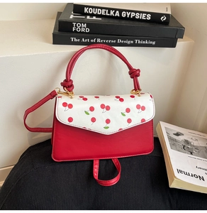 Detail of red and white crossbody bag with cherry prints and woven knot handle