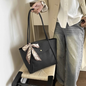 Detail of black pebbled leather tote bag with elegant silk scarf on handle for commute