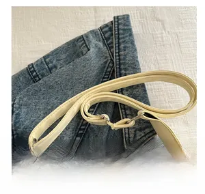 Detail of beige leather strap with stitching and metal hardware on denim background