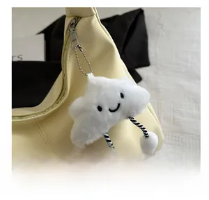 Close-up of a white plush cloud charm with a smiley face hanging on a leather handbag