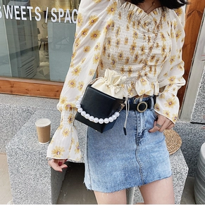 Chic black box handbag with pearl handle and crossbody chain shown on a model outdoors