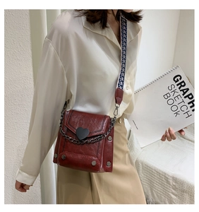 Detail of red crossbody bag with heart buckle and geometric wide woven strap