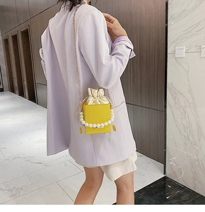 Detail of yellow bucket bag with pearl handle and cream drawstring lining on a model