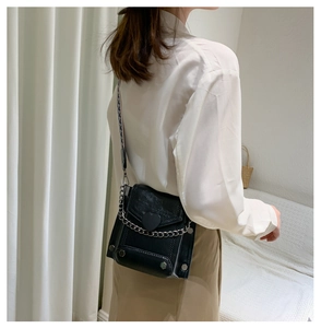 Detail of black PU leather crossbody bag with heart motif and silver chain on model