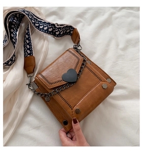 Detail of caramel leather bag with heart buckle, silver chain and ethnic woven strap