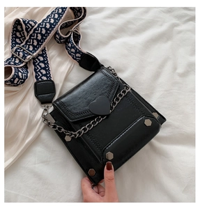 Detail of black crossbody bag with heart buckle and vintage patterned strap