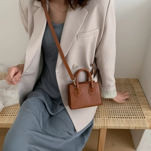 Mini caramel tote bag with top handle and shoulder strap shown in a stylish lifestyle setting