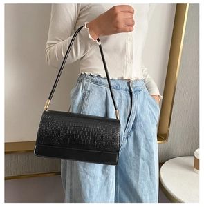 Close-up of black baguette bag featuring crocodile embossing and gold hardware details