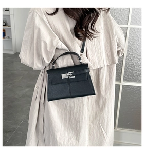 Classic black leather trapezoid bag with top handle and metal buckle shown on a model