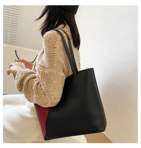 Side view of large black and red tote bag with slim straps worn by a model on shoulder