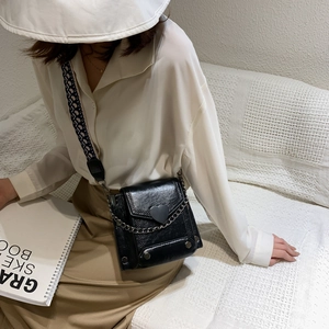 Chic black crossbody bag with heart buckle and chain strap shown on model