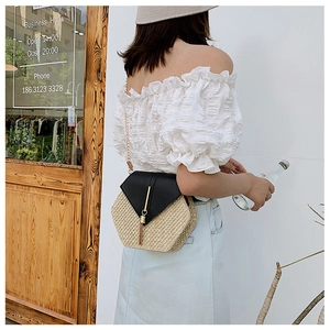 Detail view of a hexagonal straw bag with black leather flap and gold chain strap